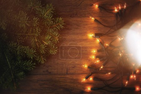Téléchargez les photos : Surface en bois ornée de lumières de Noël scintillantes et de brindilles d'épinette fraîches. - en image libre de droit