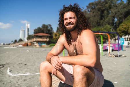 Foto de Retrato de hombre rizado alegre relajándose en la playa durante el día soleado de verano - Imagen libre de derechos
