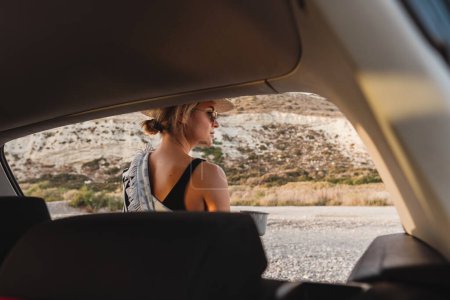 Téléchargez les photos : Voyageur femme prendre une pause avec du café par sa voiture sur une plage de galets. - en image libre de droit
