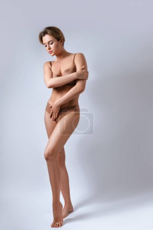 Téléchargez les photos : Portrait de jeune femme séduisante portant de la lingerie marron sur fond gris. - en image libre de droit
