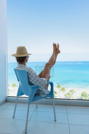 Téléchargez les photos : Jeune femme se détendre dans la chaise sur le balcon de l'hôtel en bord de mer ou appartement. - en image libre de droit