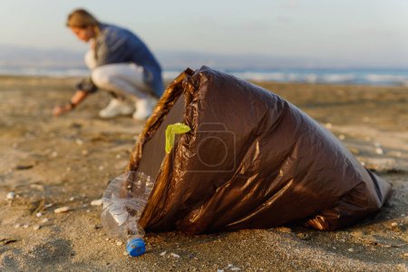 Foto de Mujer voluntaria está recogiendo residuos plásticos en la playa para contribuir al esfuerzo de mantener la naturaleza limpia. - Imagen libre de derechos
