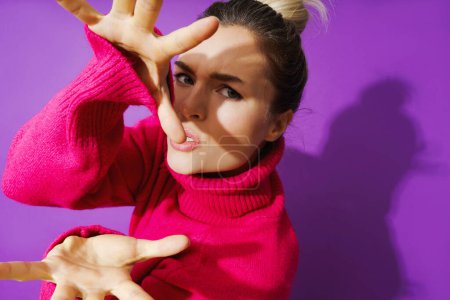 Foto de Retrato de mujer joven en pose cansada usando suéter de cuello de polo caliente sobre fondo púrpura - Imagen libre de derechos