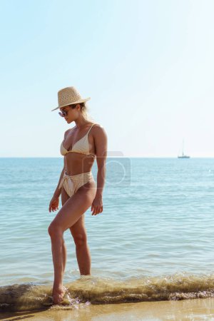 Foto de Mujer irradia vibraciones de verano vistiendo bikini de rayas amarillas y un sombrero de paja, disfrutando de su tiempo en la playa de arena. - Imagen libre de derechos