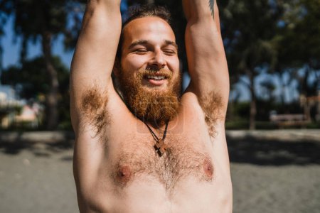 Téléchargez les photos : Jeune homme barbu échauffement avant son entraînement sur la plage - en image libre de droit