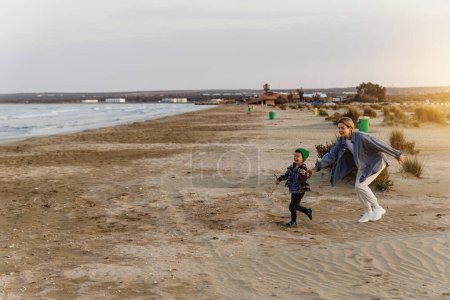 Téléchargez les photos : Jeune mère et son fils tout-petit jouer tag sur la plage au coucher du soleil. - en image libre de droit