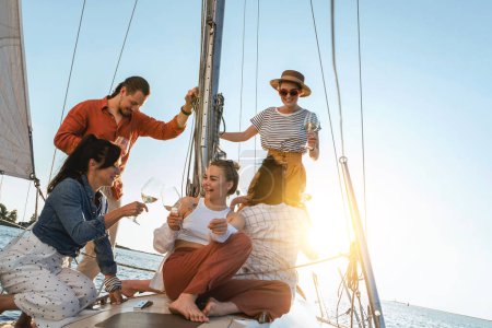 Téléchargez les photos : Groupe d'amis heureux boire du vin et se détendre sur le voilier pendant la voile en mer. - en image libre de droit