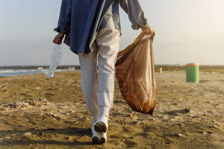 Téléchargez les photos : Femme bénévole collecte des déchets plastiques sur la plage pour contribuer à l'effort de garder la nature propre. - en image libre de droit