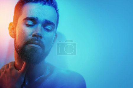 Téléchargez les photos : Portrait de beau jeune homme au visage mouillé en lumière bleue et orange - en image libre de droit