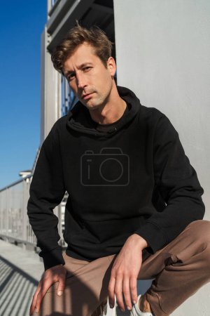 Foto de Retrato de un joven adulto serio en la calle con espacio en blanco en su sudadera con capucha negra - Imagen libre de derechos