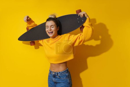 Foto de Retrato de niña alegre con longboard sobre fondo amarillo - Imagen libre de derechos