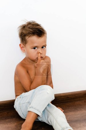 Foto de Lindo niño metiendo la nariz y sentado en el suelo. - Imagen libre de derechos