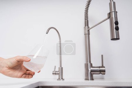 Photo for Woman get filtered water from stainless faucet into a glass. - Royalty Free Image