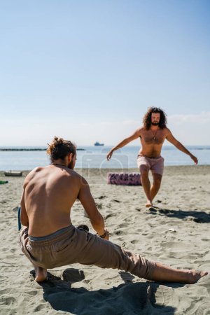 Foto de Dos hombres se calientan antes del entrenamiento de calistenia en la playa de arena - Imagen libre de derechos