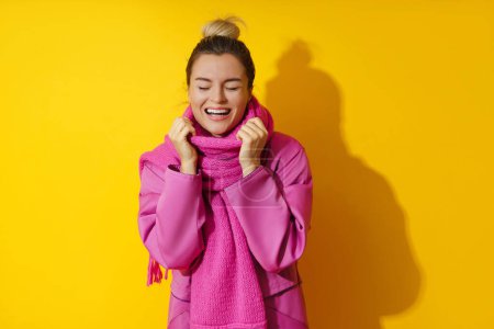 Foto de Retrato de una joven mujer alegre con abrigo rosa y bufanda de lana sobre fondo amarillo - Imagen libre de derechos
