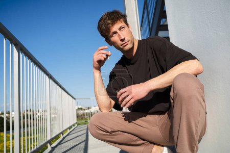 Téléchargez les photos : Jeune homme adulte fumant et buvant de l'alcool près du complexe d'appartements - en image libre de droit