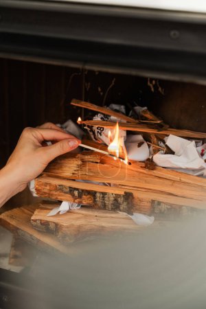 Téléchargez les photos : Main féminine tient une allumette, prête à enflammer le bois de chauffage dans une cheminée. - en image libre de droit