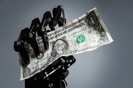 Foto de Mano robótica real con un billete de un dólar. Conceptos de inversión en tecnología de inteligencia artificial o sustitución de puestos de trabajo por IA. - Imagen libre de derechos