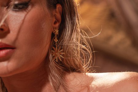 Foto de Mujer joven, su belleza acentuada por pendientes dorados en forma intrincada como las estrellas y el sol. - Imagen libre de derechos