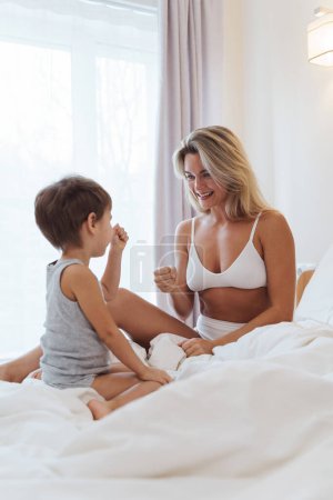 Photo for Happy mother and her little son engage in cheerful play, creating precious memories as they bond in the comfort of their bed. - Royalty Free Image