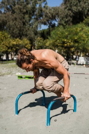 Foto de Joven haciendo handstand para la fuerza y el equilibrio en las barras paralelas durante el entrenamiento en la playa - Imagen libre de derechos