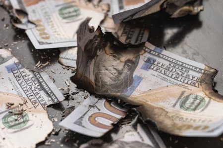 Foto de Los restos de billetes quemados de cien dólares reducidos a cenizas simbolizan el concepto de una crisis económica, inflación y fracaso empresarial.. - Imagen libre de derechos
