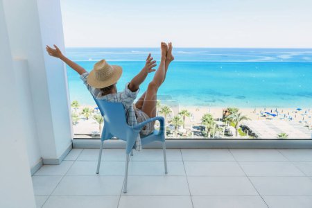 Photo for Young woman relaxing in chair on balcony of beachfront hotel or apartment. - Royalty Free Image