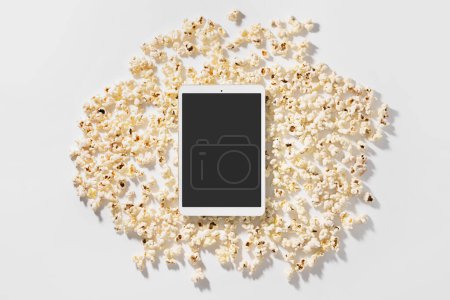 Foto de Dispersa deliciosas palomitas de maíz y tableta con pantalla en blanco para su diseño - Imagen libre de derechos