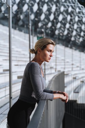 Photo for Portrait of confident woman athlete wearing female sportswear on bleachers in outdoor stadium. - Royalty Free Image