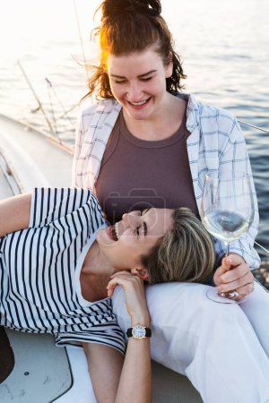 Téléchargez les photos : Deux filles buvant du vin et se relaxant sur le voilier pendant la voile dans la mer. - en image libre de droit