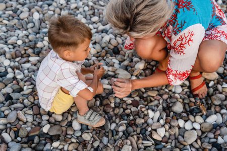 Photo for Mother and her cute little son collecting pebbles on shingle beach. - Royalty Free Image