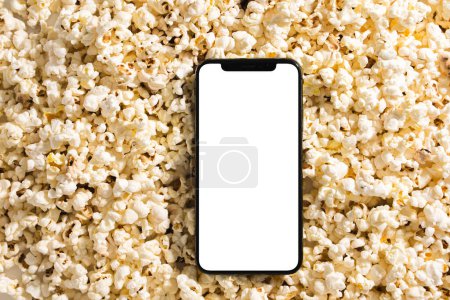 Foto de Deliciosas palomitas de maíz y smartphone con pantalla en blanco para su diseño. - Imagen libre de derechos