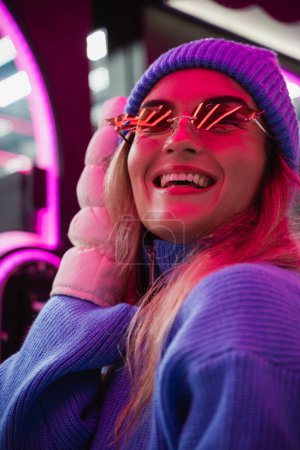 Téléchargez les photos : Femme gaie et élégante, vêtue de vêtements chauds et portant des lunettes de soleil en forme de flammes de feu, s'amuse dans un parc d'attractions hivernal enneigé. - en image libre de droit