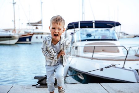 Téléchargez les photos : Garçon élégant excité courir près du yacht dans la marina. - en image libre de droit