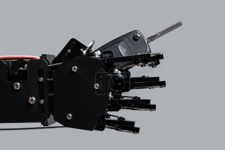 Téléchargez les photos : Véritable main robotique avec clé de voiture noire. Concept d'intelligence artificielle dans l'industrie des transports. - en image libre de droit
