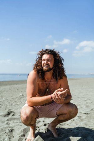 Téléchargez les photos : Portrait de l'homme bouclé se détendre sur la plage pendant la journée ensoleillée d'été - en image libre de droit