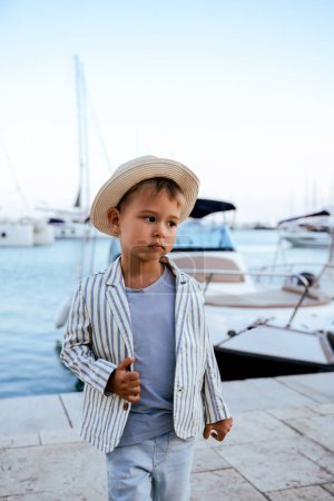 Photo for Portrait of cute stylish boy posing near yacht in marina - Royalty Free Image