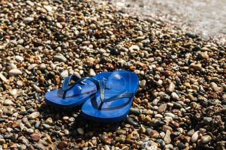 Foto de Primer plano de chanclas de caucho azul húmedo en la playa de guijarros - Imagen libre de derechos