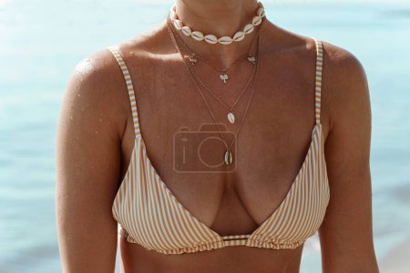 Photo for Closeup of female neck with golden necklace with palm trees and seashells on a sunlit beach. - Royalty Free Image