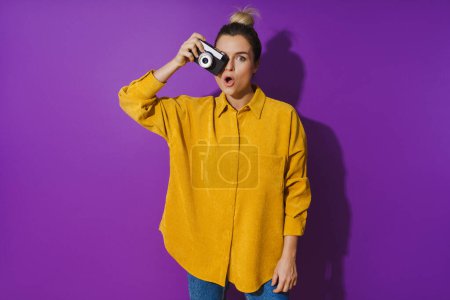 Photo for Portrait of young surprised girl with film photo camera on purple background - Royalty Free Image