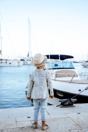 Téléchargez les photos : Portrait de garçon élégant mignon posant près du yacht dans la marina - en image libre de droit