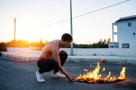 Téléchargez les photos : Jeune homme adulte pyromane brûlant sa chemise dans la rue - en image libre de droit