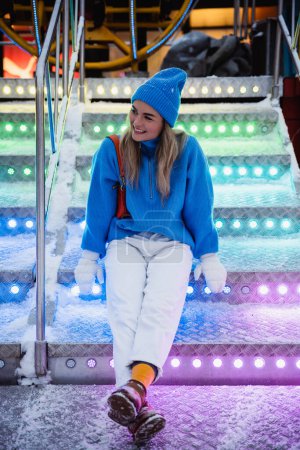 Foto de Mujer alegre y elegante, vestida con ropa de abrigo, se divierte en un parque de atracciones de invierno nevado. - Imagen libre de derechos