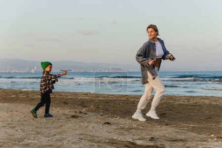 Téléchargez les photos : Jeune mère et son fils tout-petit jouer tag sur la plage au coucher du soleil. - en image libre de droit