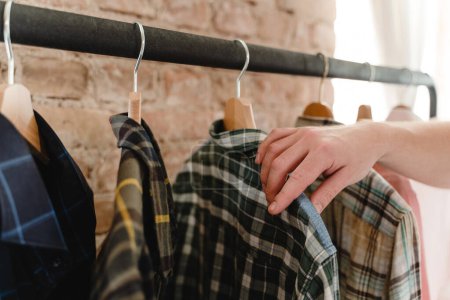 Photo for Man is browsing through his various shirts hanging on the clothing rack in the wardrobe - Royalty Free Image