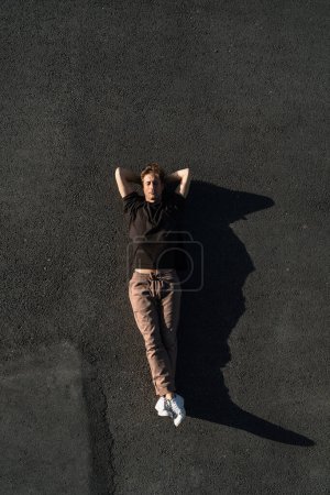 Photo for Top view of young adult man carefree lying on the asphalt - Royalty Free Image