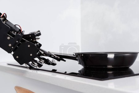 Téléchargez les photos : Véritable robot main et poêle à frire sur cuisinière électrique. Concept d'automatisation robotique des processus. - en image libre de droit