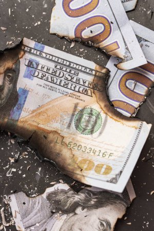 Photo for The remains of burnt one hundred dollar bills reduced to ashes symbolize the concept of an economic crisis, inflation, and business failure. - Royalty Free Image