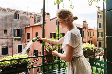 Junge Frau gießt Pflanzen auf winzigem Balkon mit Gießspray