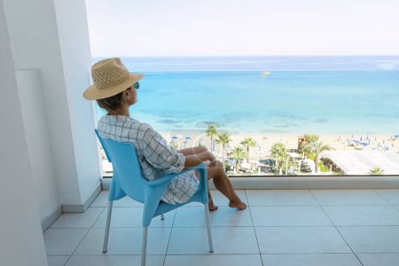 Foto de Mujer joven relajándose en silla en el balcón del hotel o apartamento frente al mar. - Imagen libre de derechos